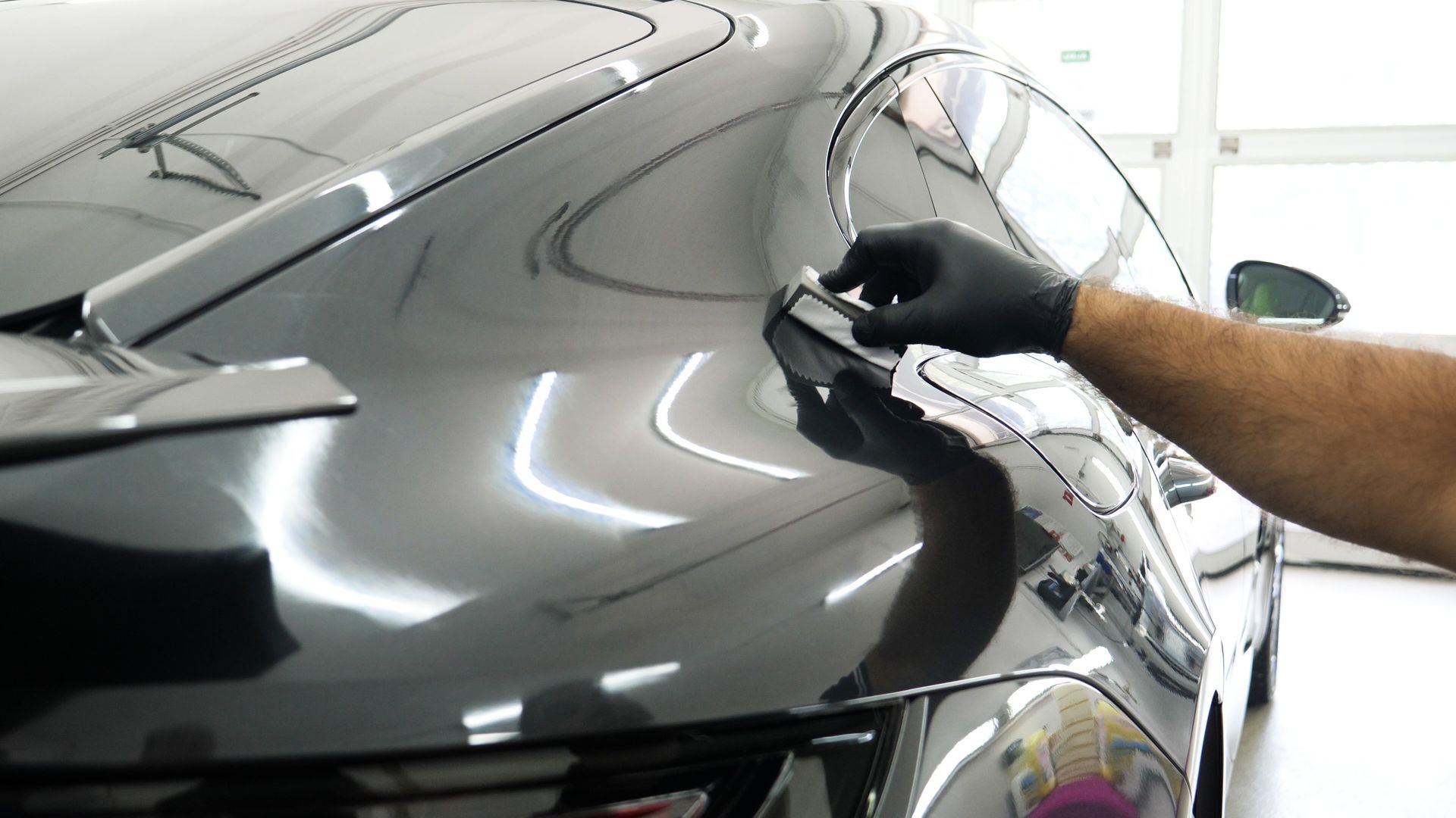 A man is polishing the hood of a black car.