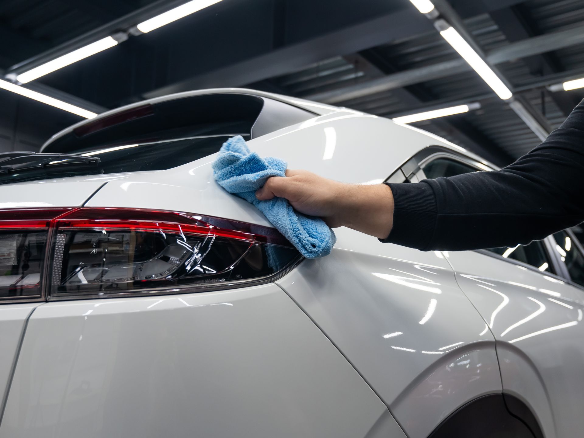 A person is cleaning a white car with a blue cloth.
