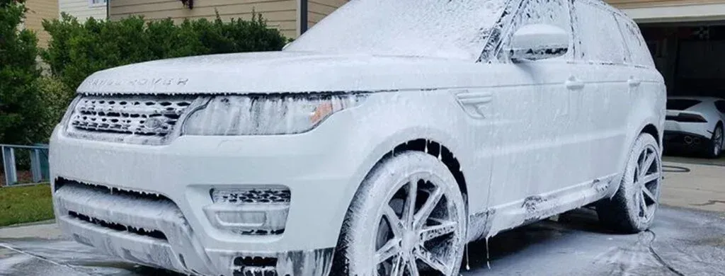 A white suv is covered in foam in a driveway.