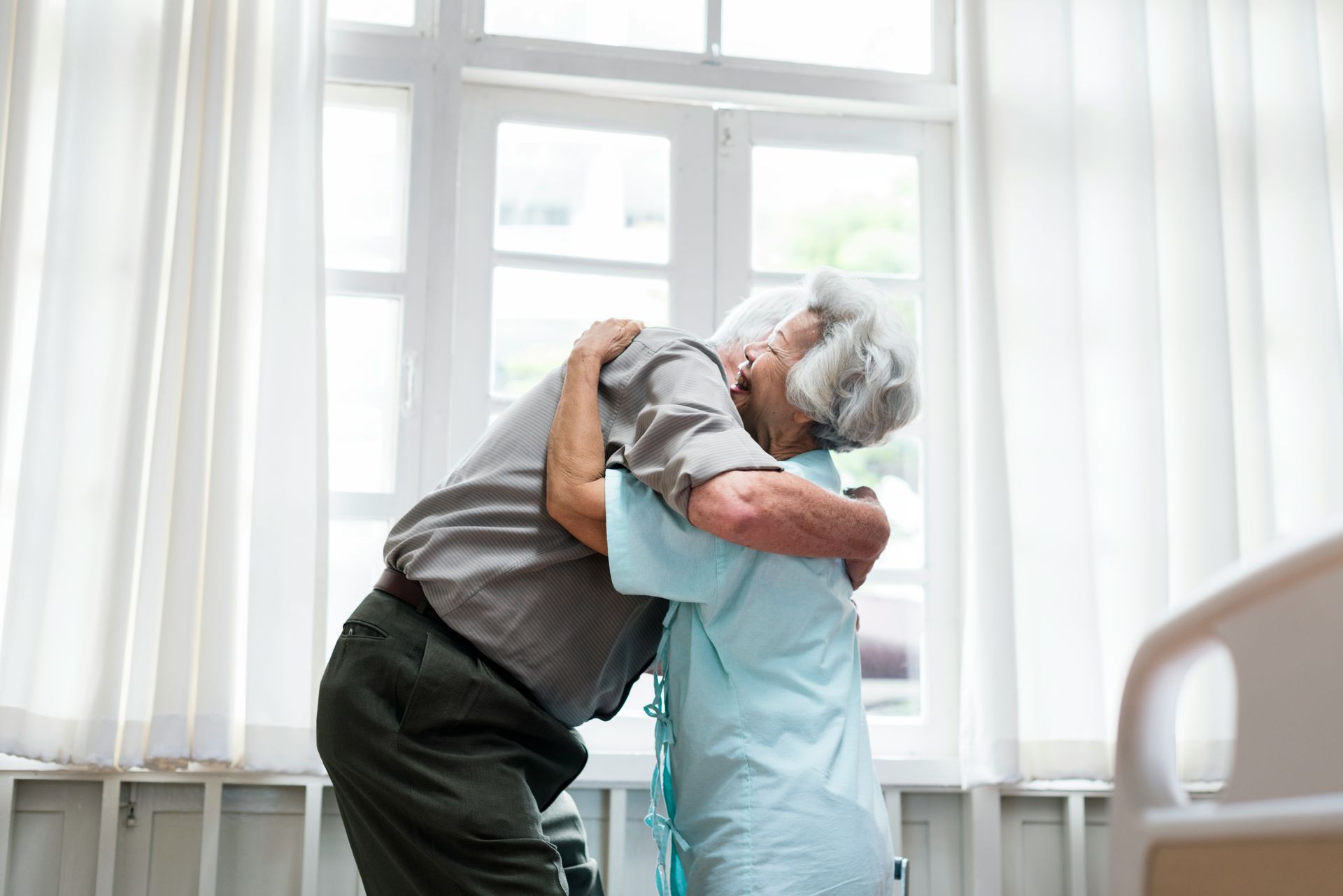 An elderly couple hugging each other in a hospital room.