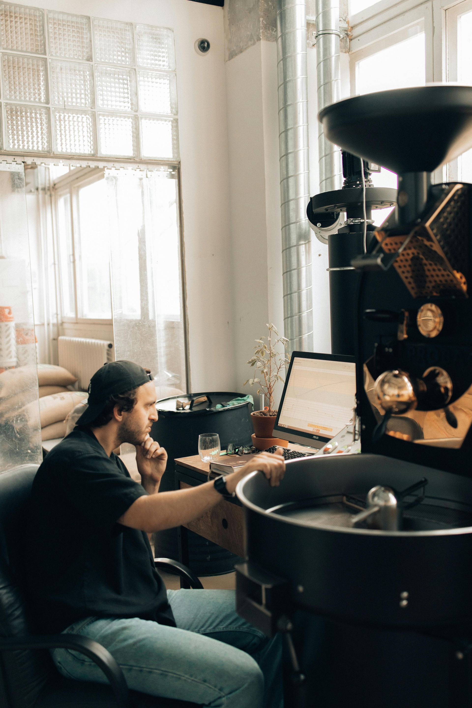 A man is sitting at a desk in front of a coffee roaster.