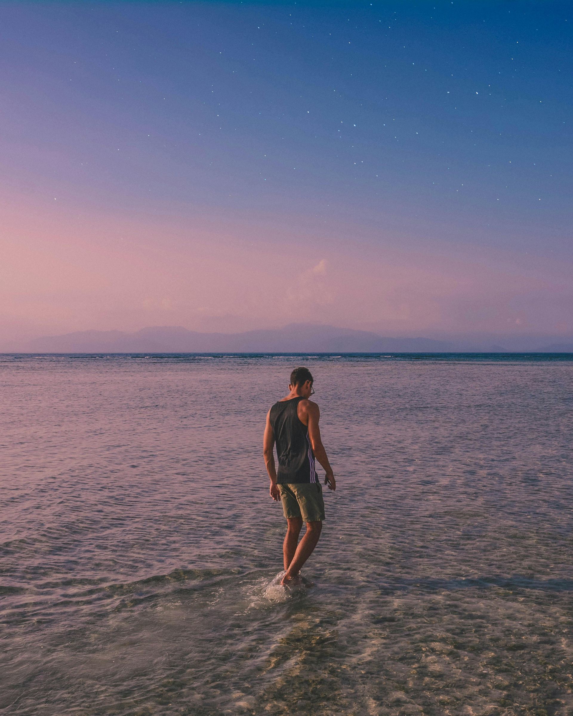 A man is walking in the ocean at sunset.
