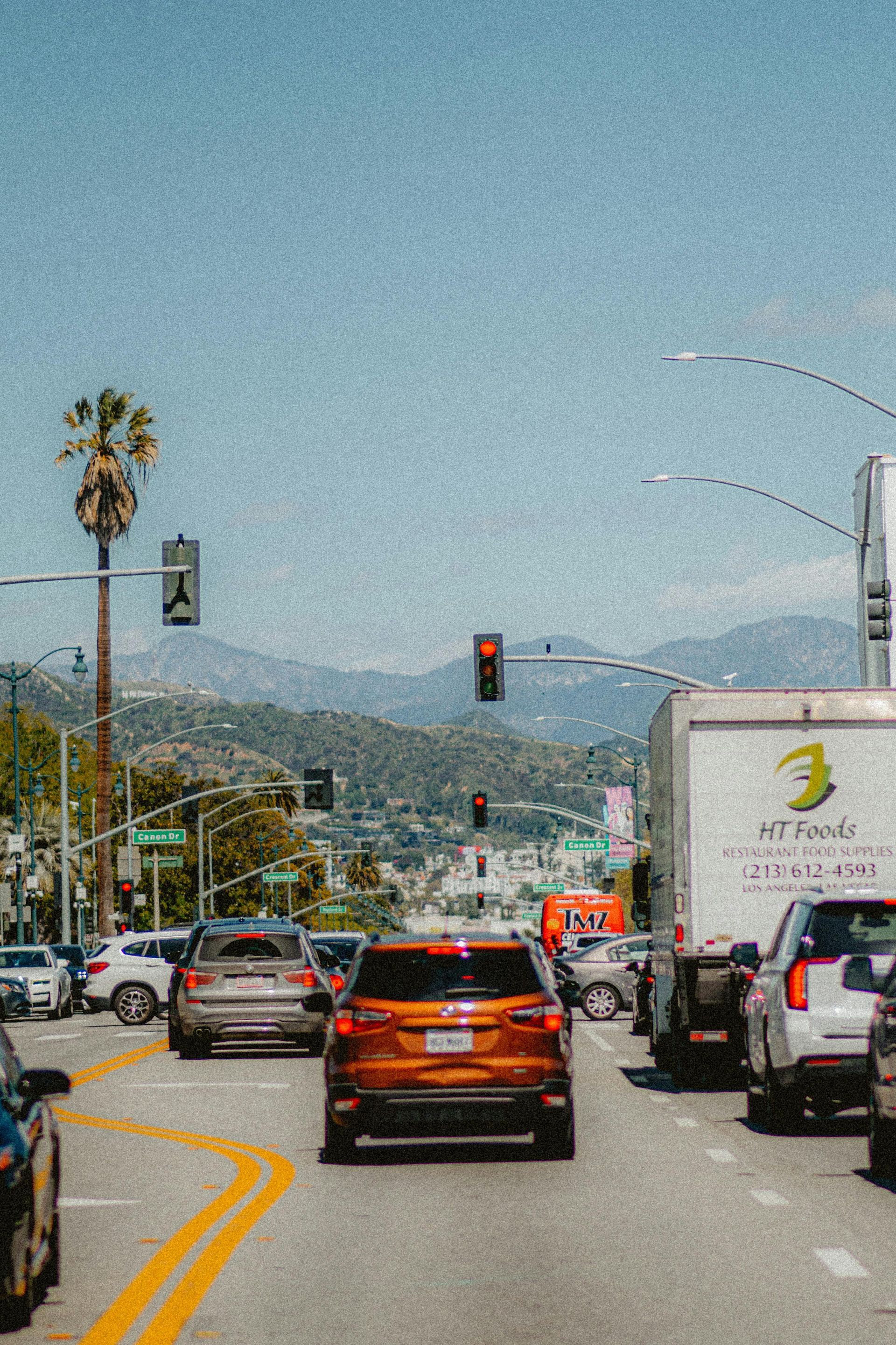 A lot of cars are driving down a busy street with mountains in the background.