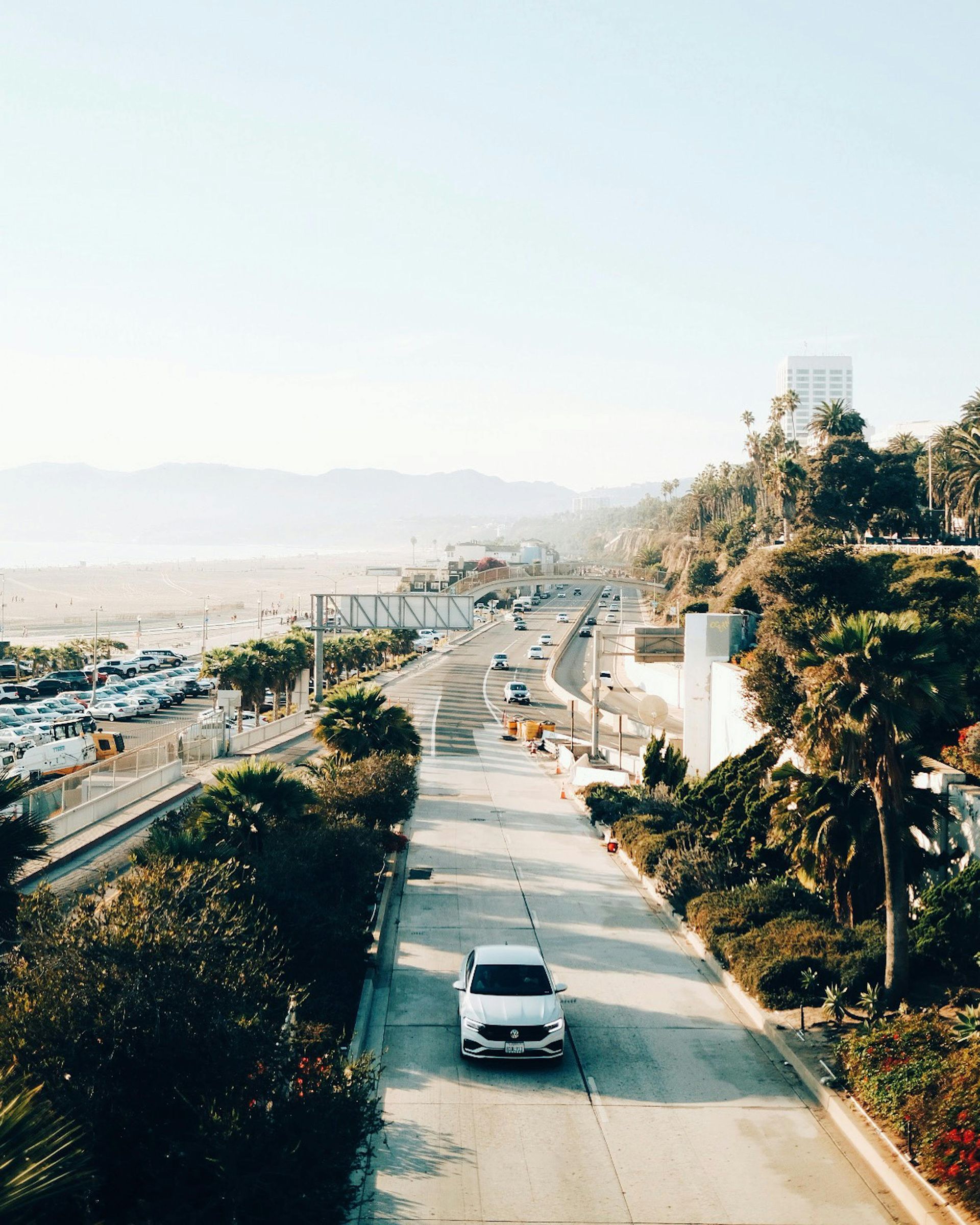 A white car is driving down a highway surrounded by trees.