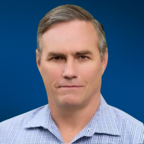 A man in a plaid shirt is standing in front of a blue background.