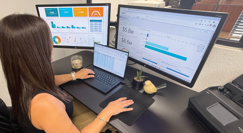 A woman is sitting at a desk with a laptop and two monitors.