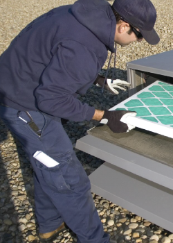 A man in a blue hoodie is working on an air conditioning unit replacing a filter