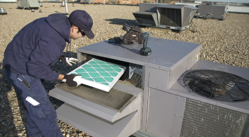 A man is working on an air conditioner on the roof of a building.
