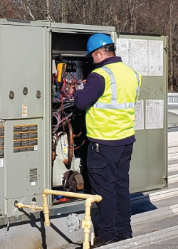 A man wearing a hard hat and safety vest is working on a machine.