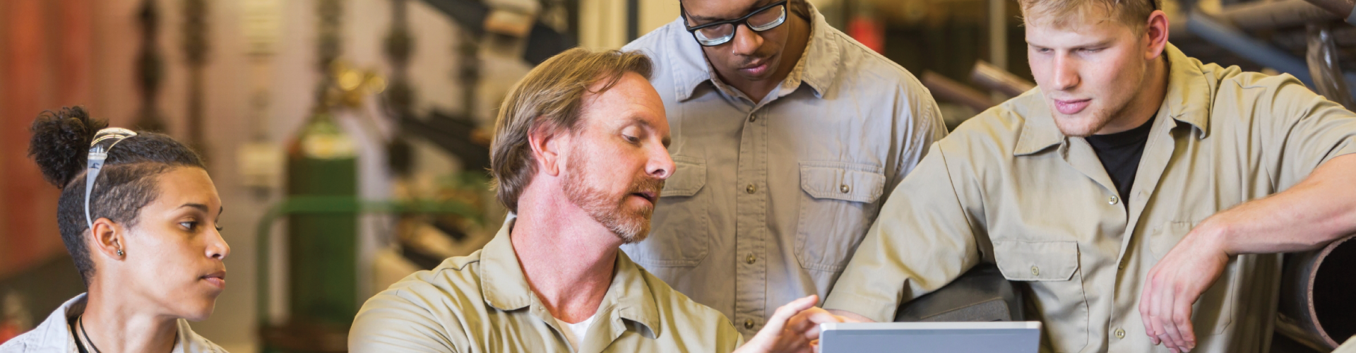 A group of workers are looking at a tablet computer in a factory.