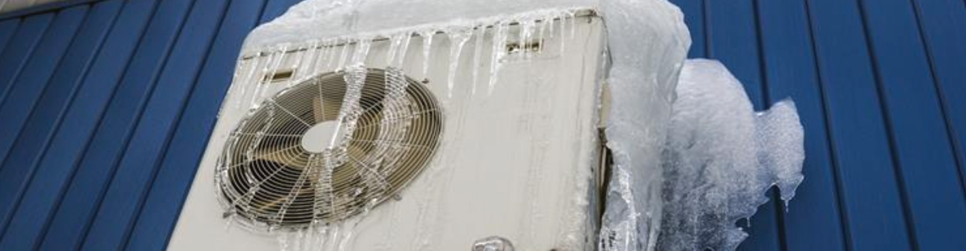 A white air conditioner is covered in ice on a blue building.
