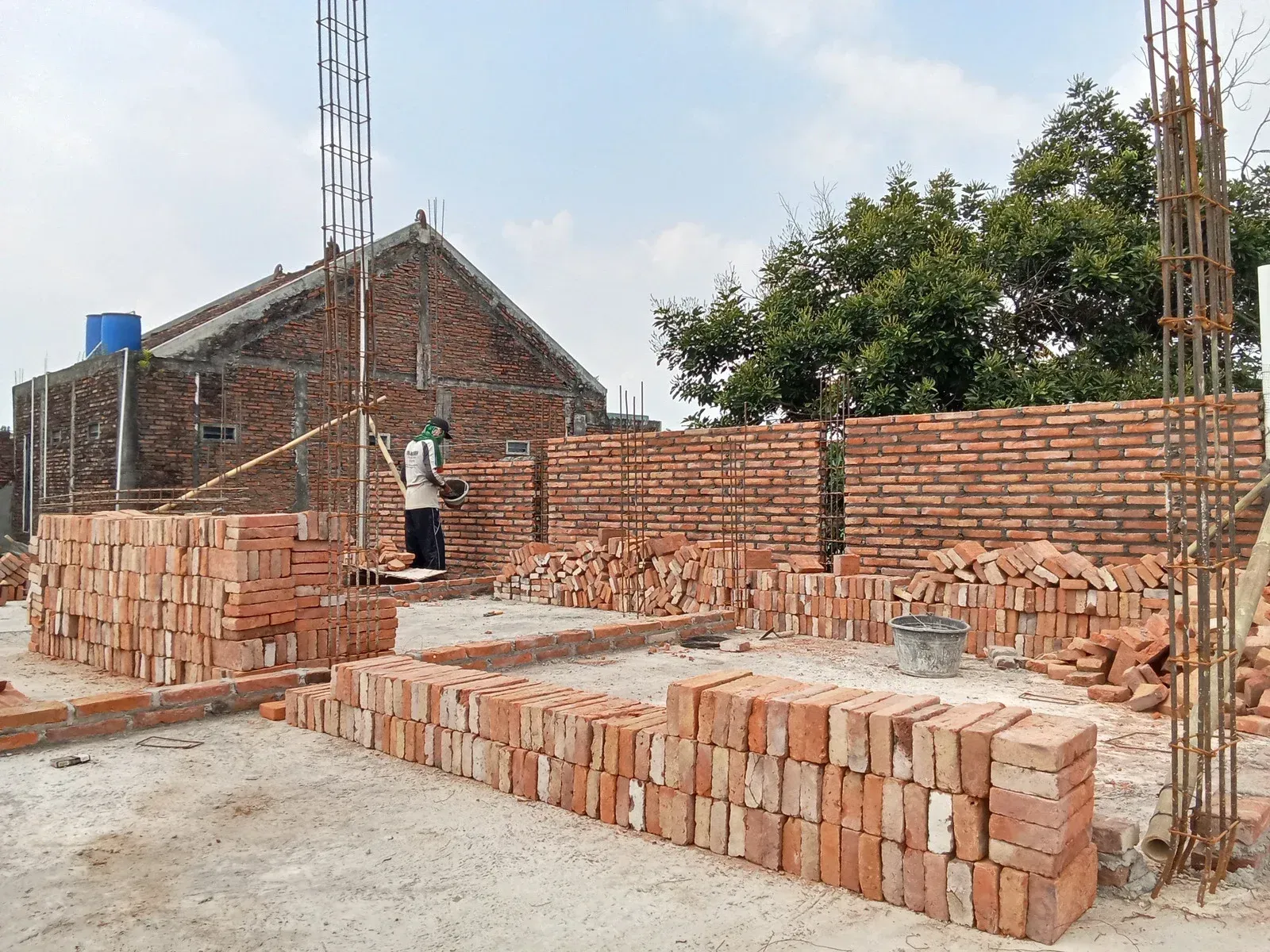 Construction site with brick walls and stacked bricks; worker nearby.