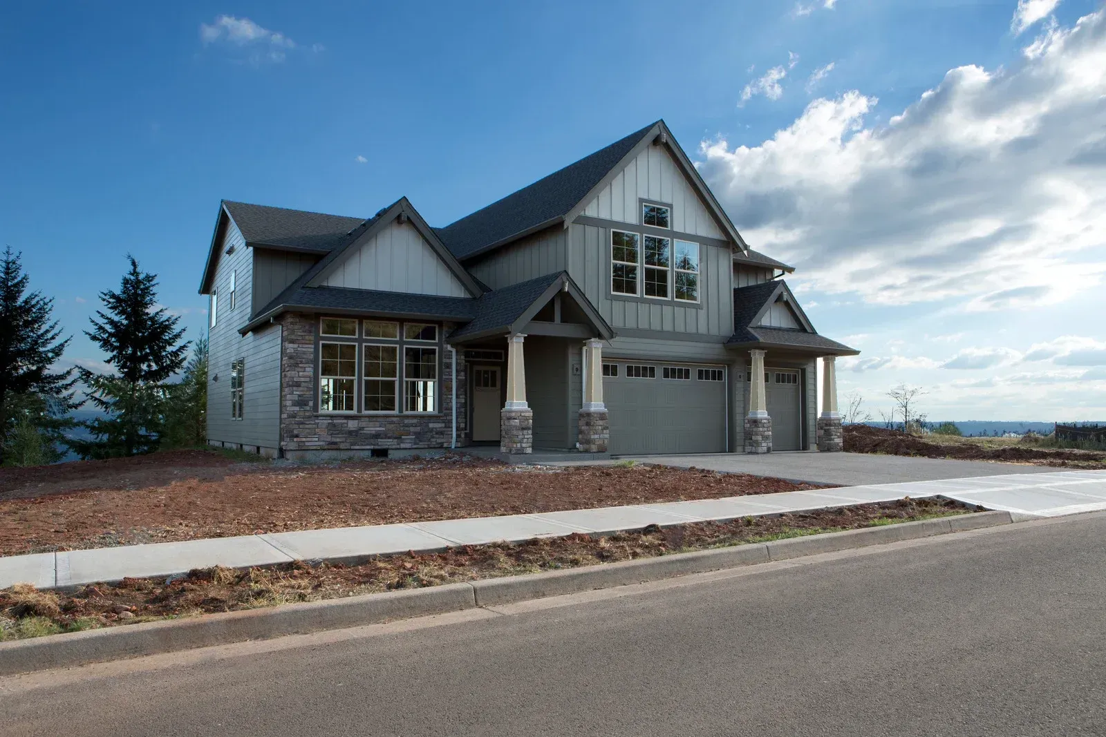 Two-story house with gray siding, stone accents, and two-car garage under a blue sky.