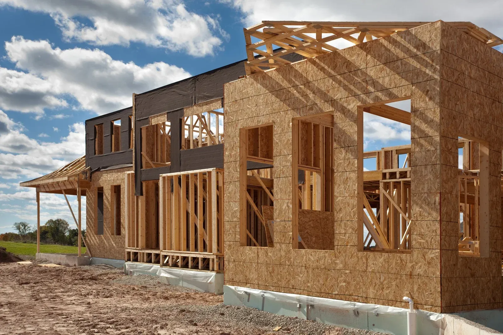 Wooden house under construction with framing and sheathing visible against a cloudy sky.