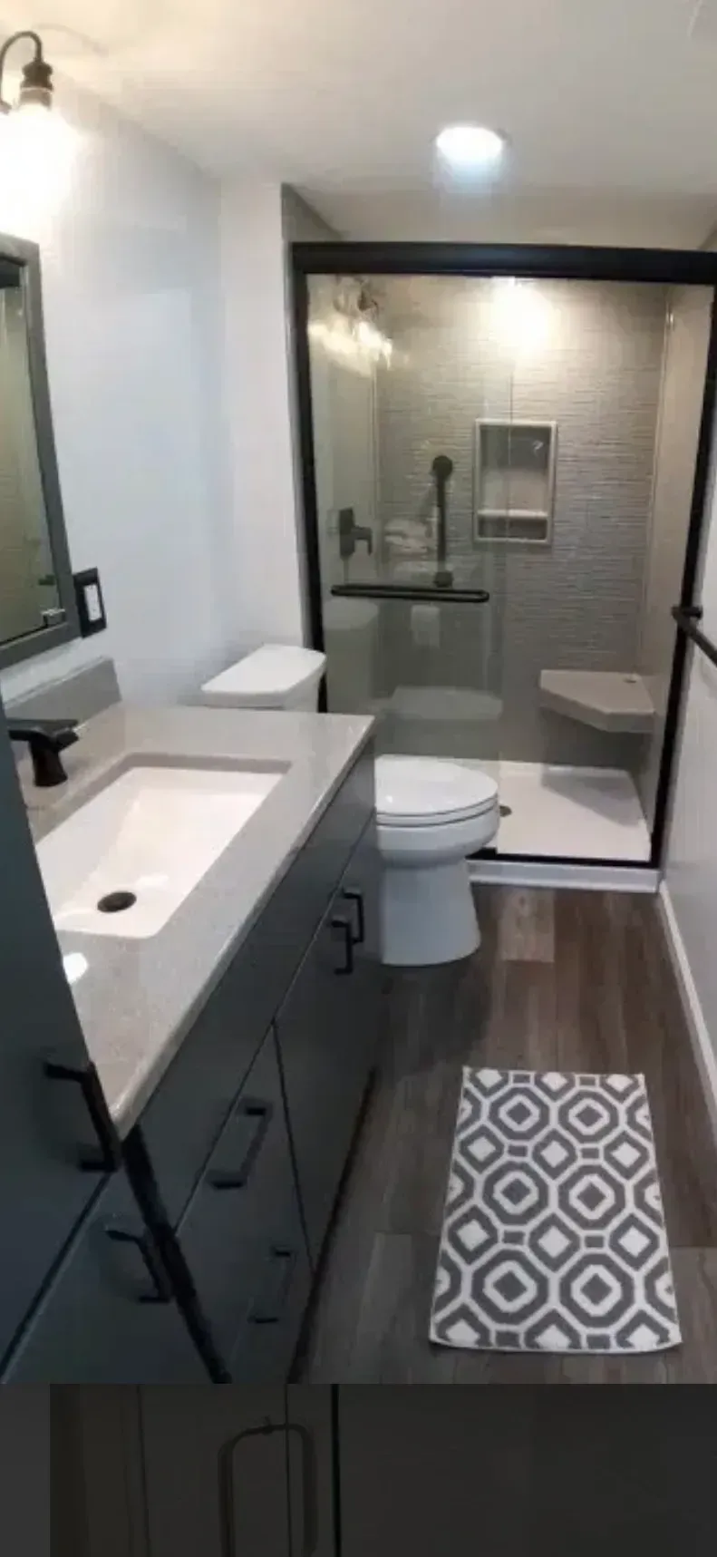 Modern bathroom with gray vanity, shower, and toilet; gray patterned floor mat.