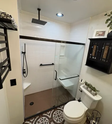 Bathroom with glass shower, black fixtures, white tile, toilet, and decorative floor.