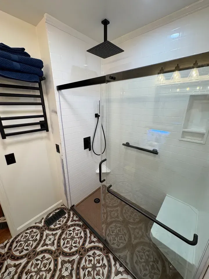 Modern bathroom with a glass-enclosed shower, patterned floor, and black fixtures.