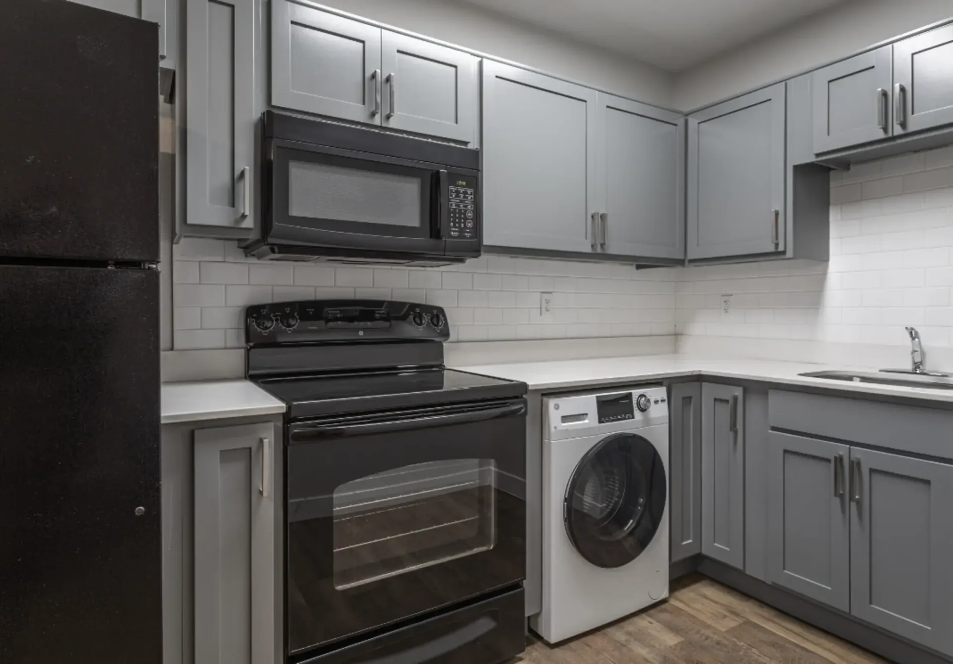 a kitchen with gray cabinets and black appliances including a washer and dryer