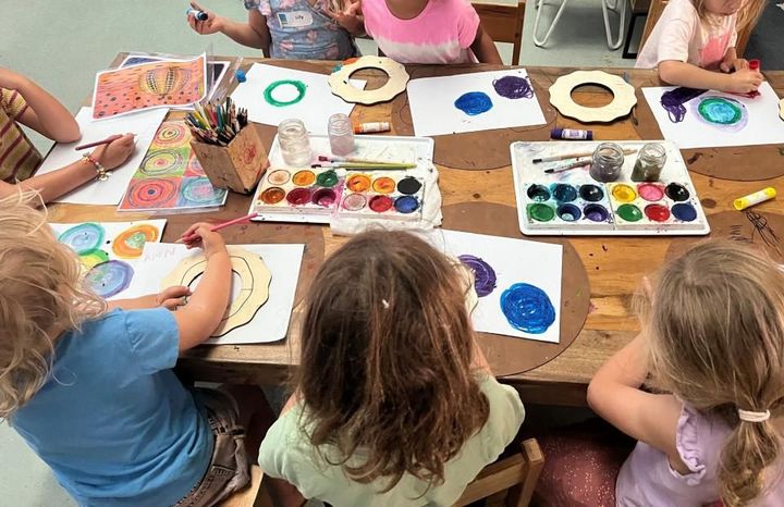 A group of children are sitting at a table painting with watercolours.