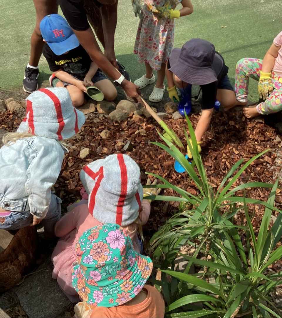 A group of children are playing with a shovel in a garden.