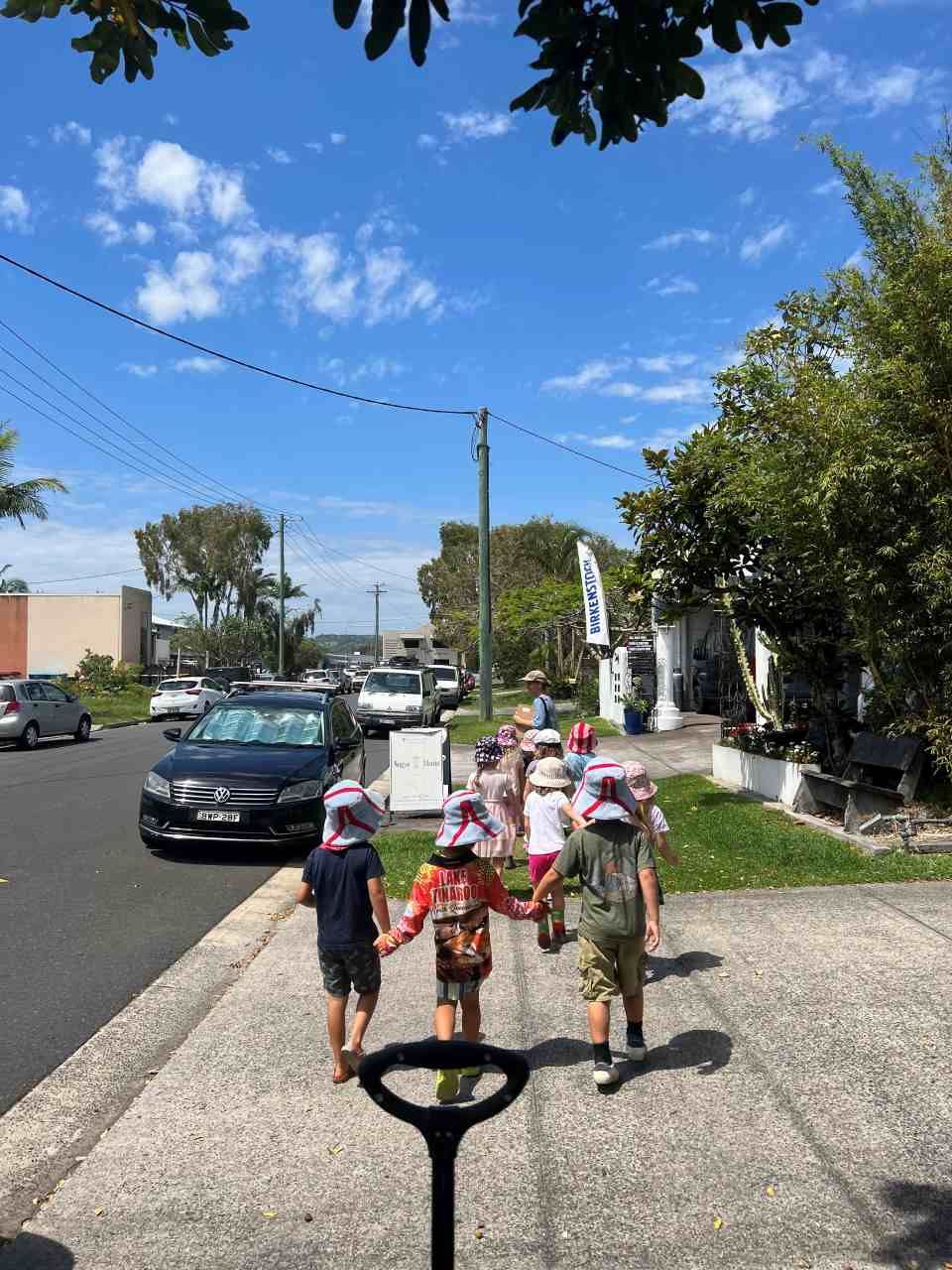 A group of children are walking down a sidewalk holding hands.