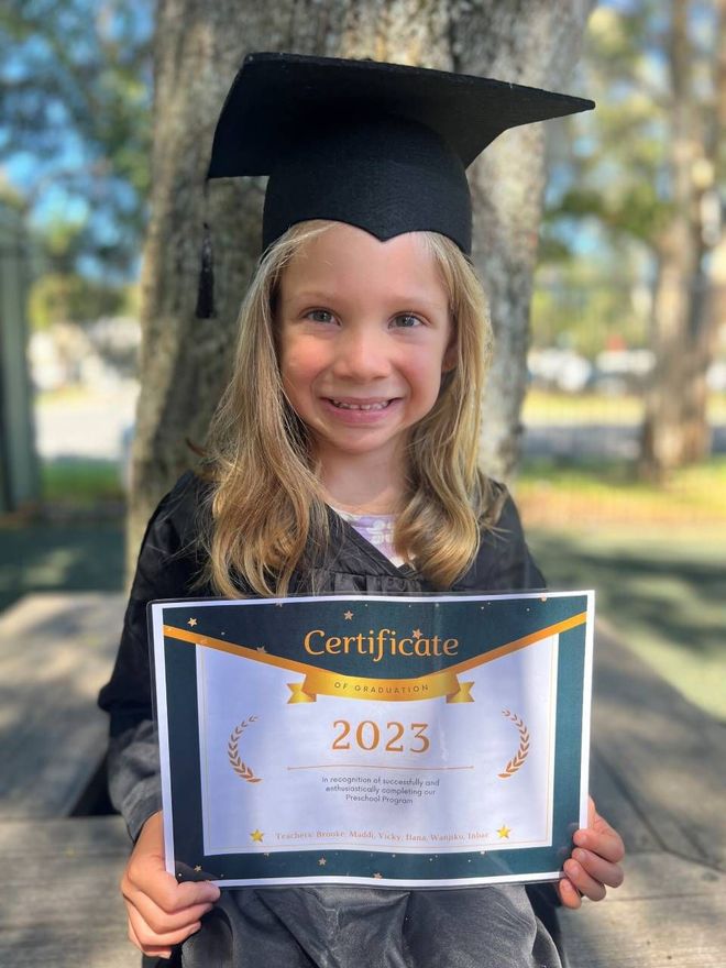 A little girl in a graduation cap and gown is holding a certificate.