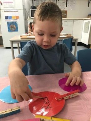 A young boy is sitting at a table playing with clothespins.