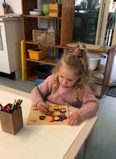 A little girl is sitting at a table drawing on a piece of paper.