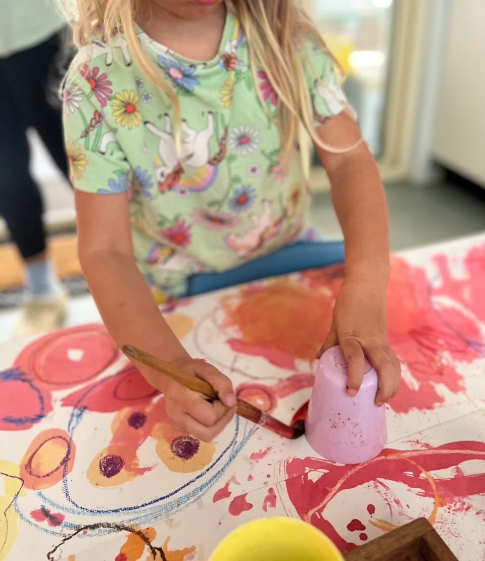 A little girl is sitting at a table painting with a brush