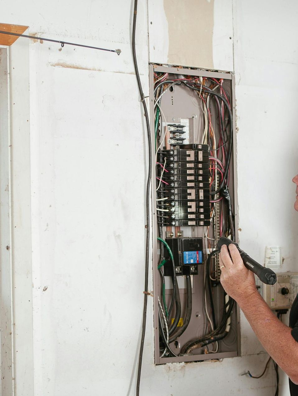 A man is working on an electrical box on a wall.