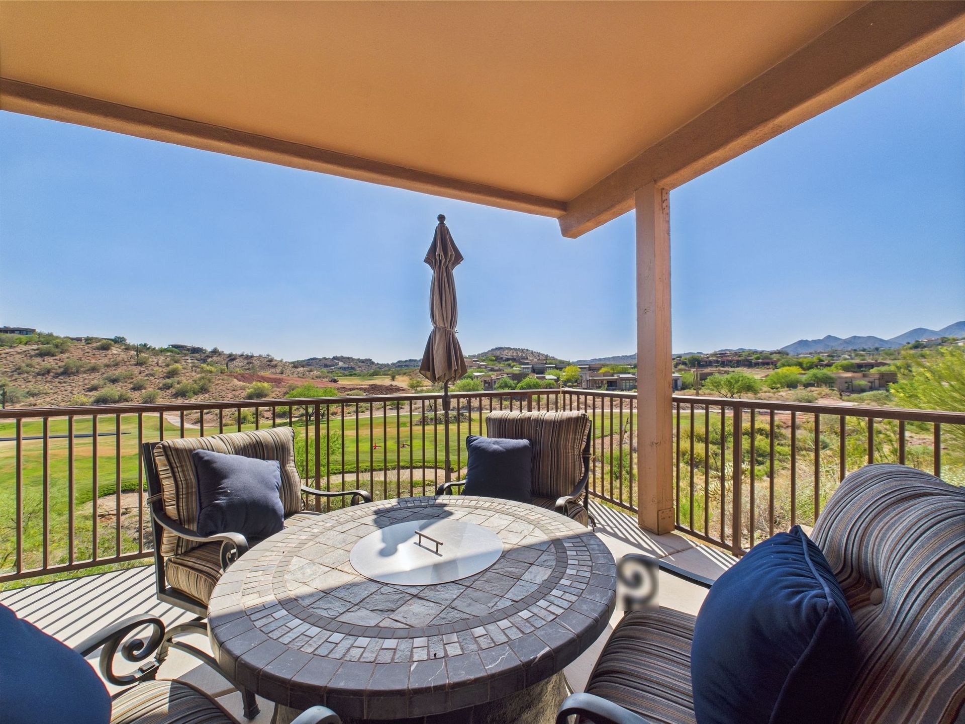 Patio with table, chairs, and umbrella overlooking a valley under a blue sky.