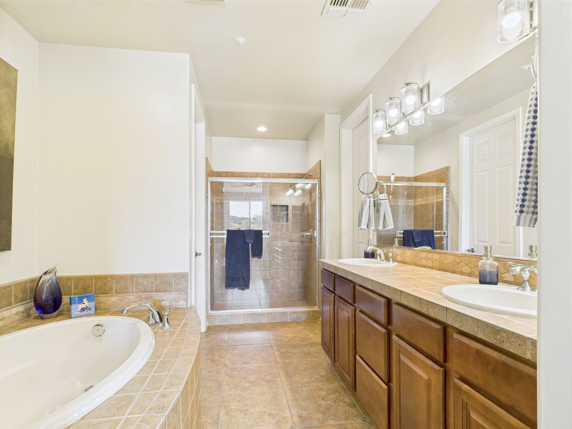Spacious bathroom with a tub, shower, double vanity, and brown cabinets.