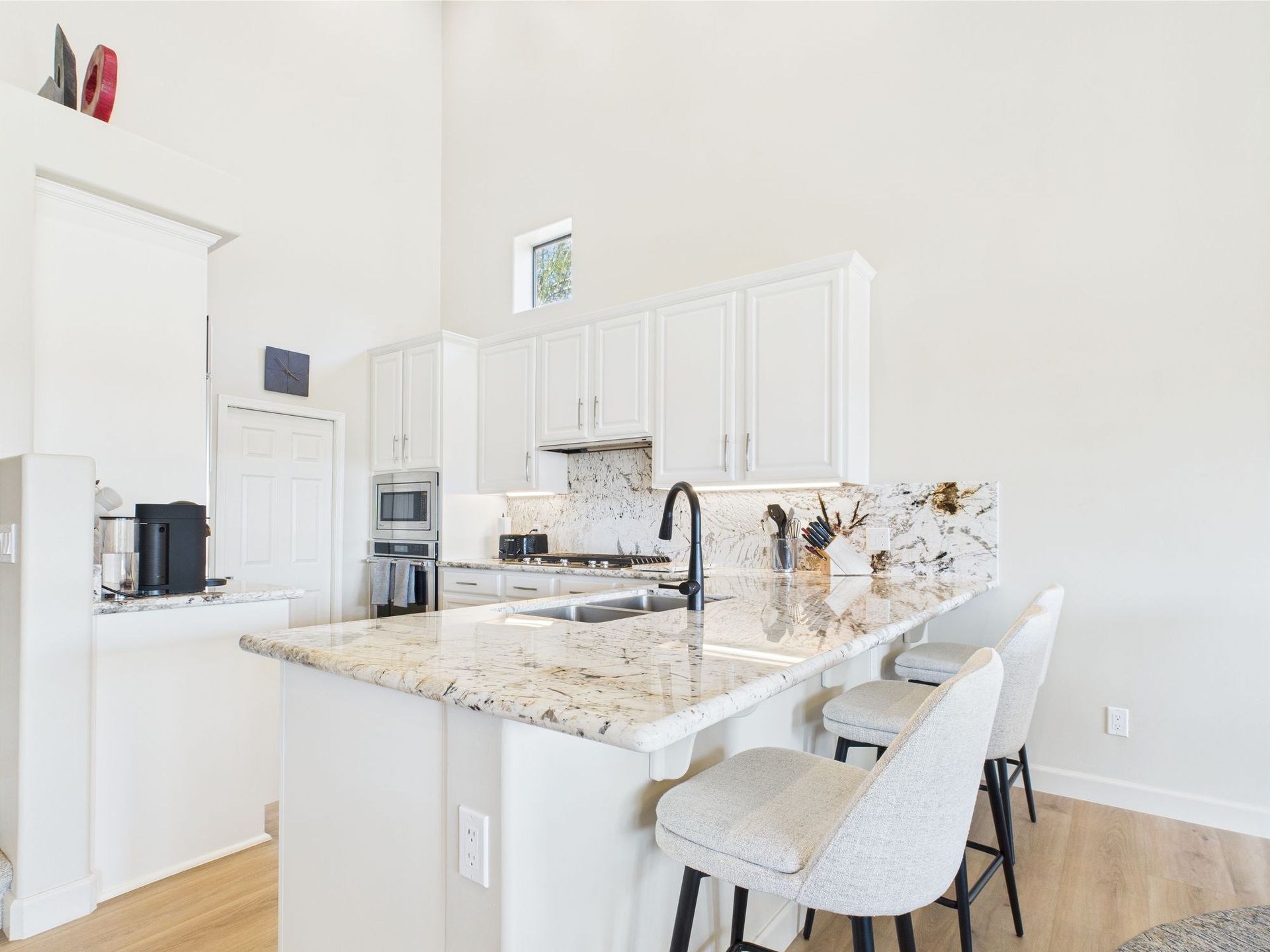 White kitchen with island seating, granite countertop, and stainless steel appliances.