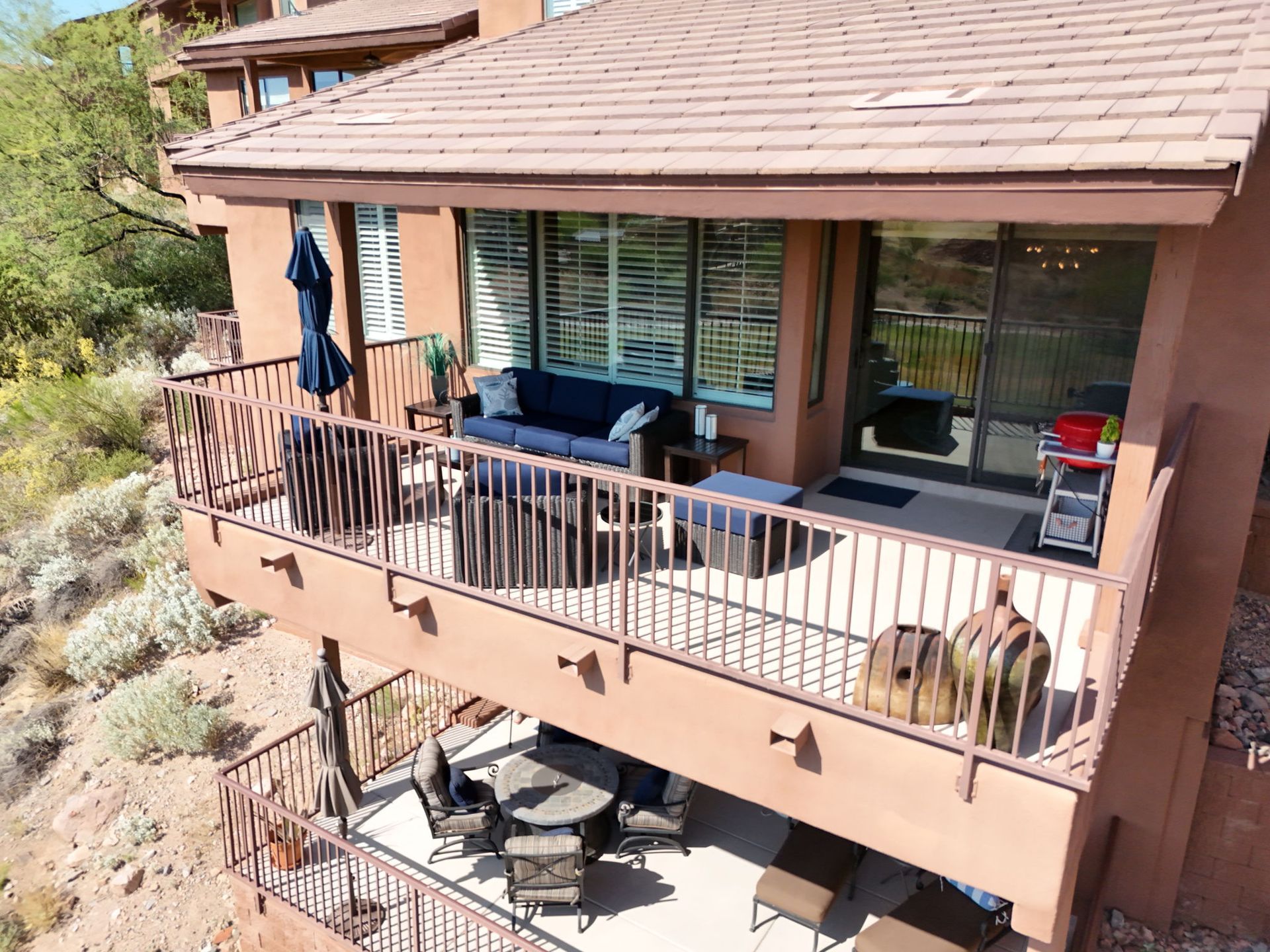 Two-story balcony overlooking hillside; upper level has seating and sofa, lower level with table and chairs.