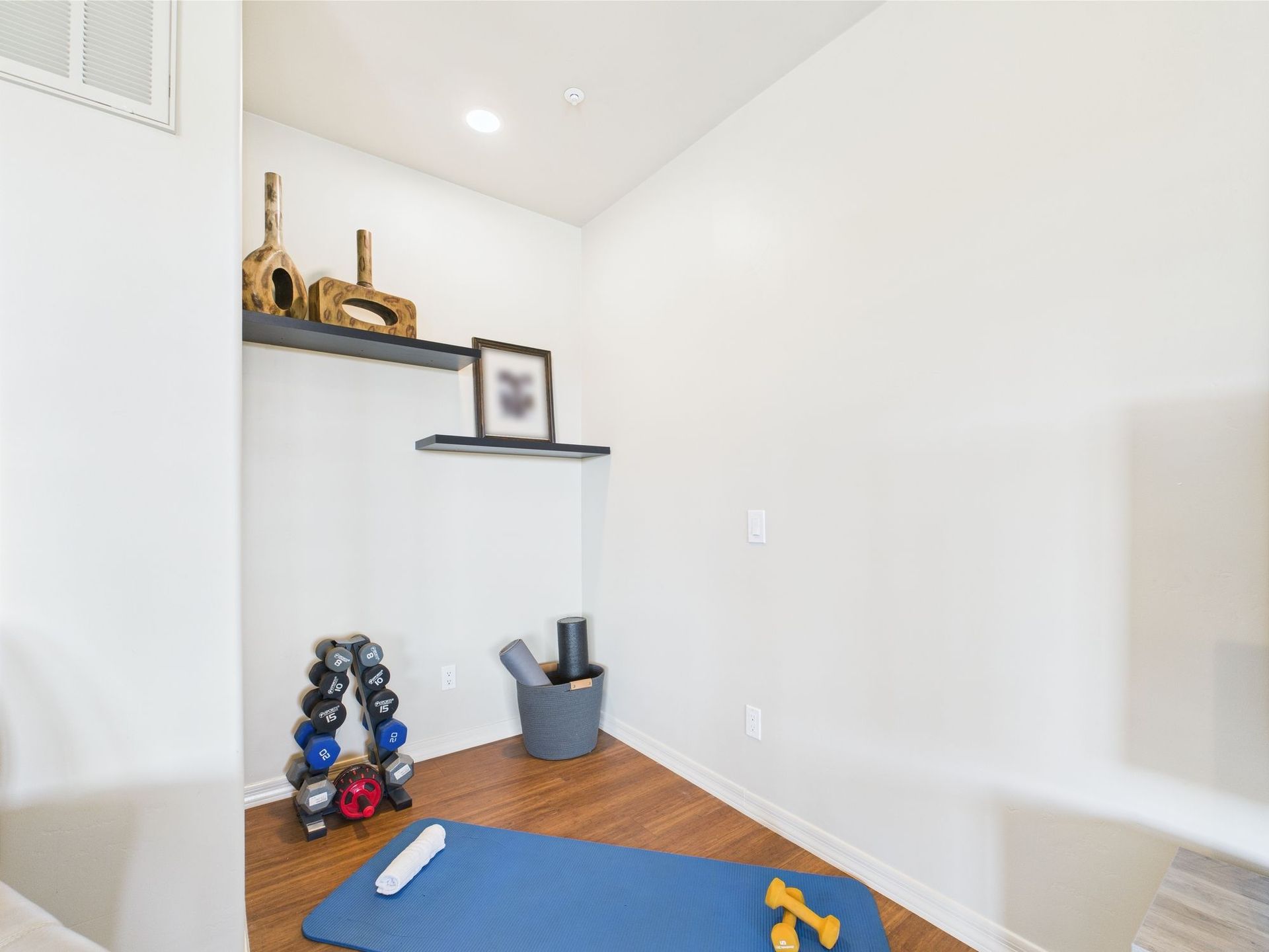 Home gym with weights, mat, and shelves in a small, light-filled space.