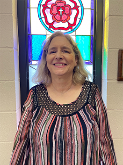 A woman in a striped shirt is smiling in front of a stained glass window.