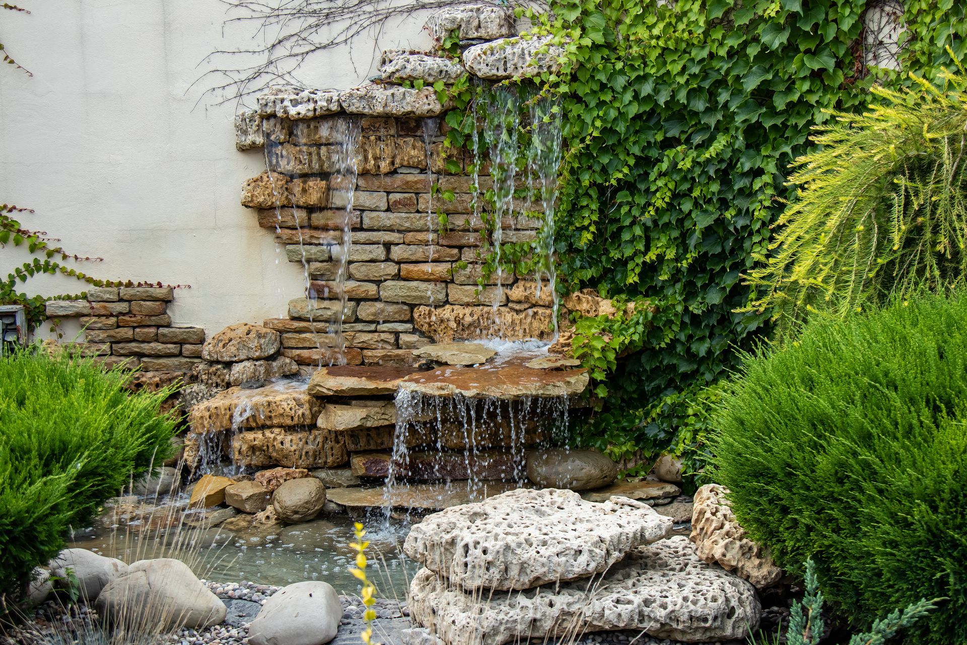 There is a waterfall in the middle of a garden made of travertine and brick