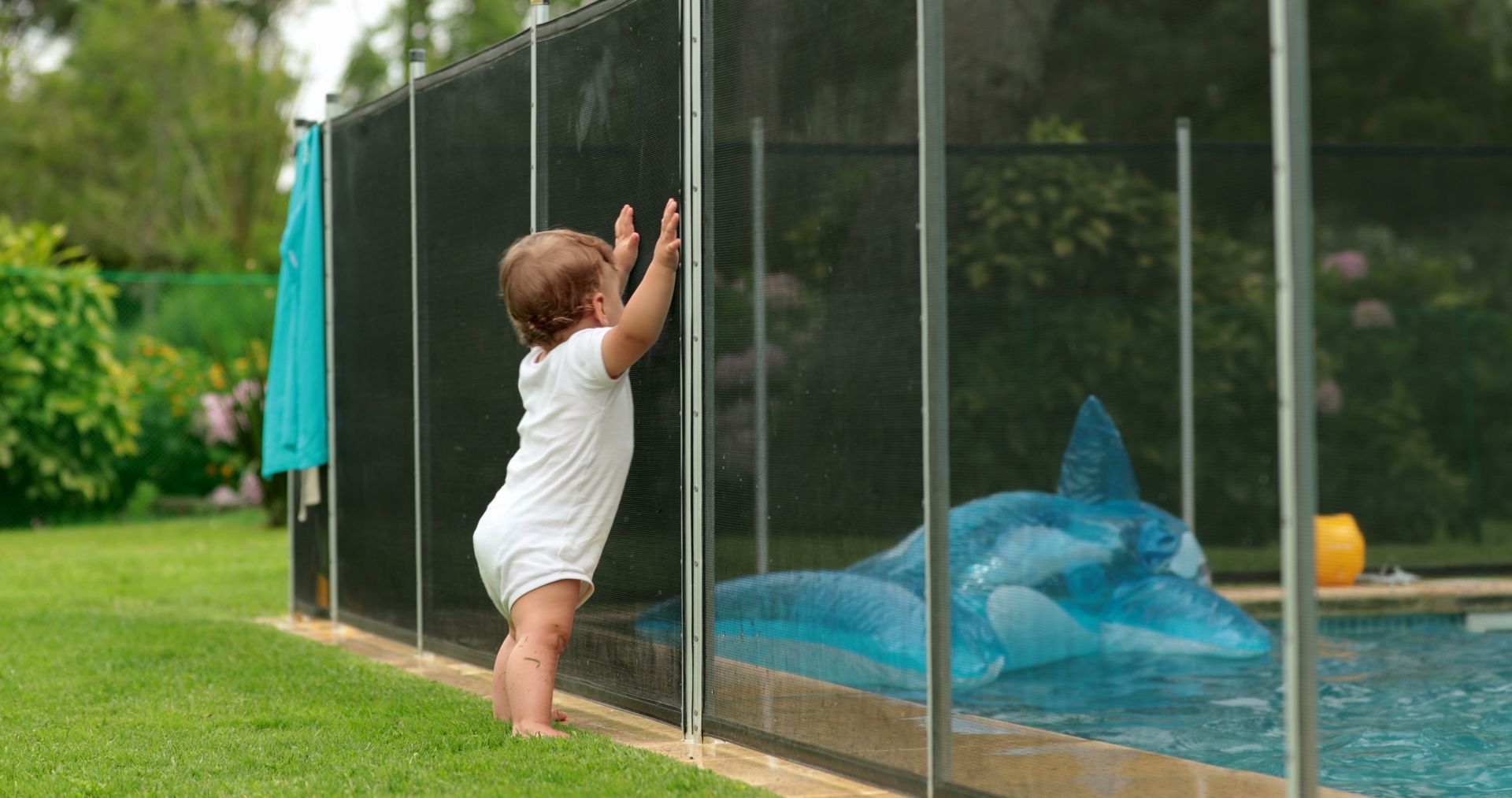 baby standing outside with hands on a pool fence