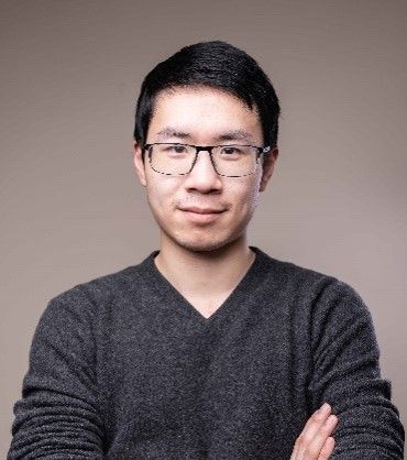 A man wearing glasses and a sweater is standing with his arms crossed.