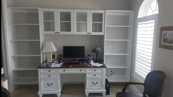 A desk with a computer on it is surrounded by shelves and cabinets.