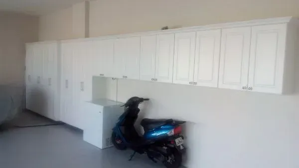 A motorcycle is parked in a garage with white cabinets.