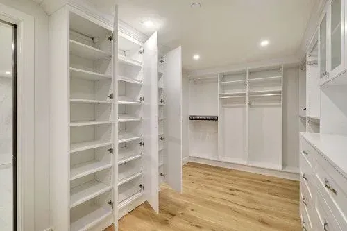 A walk in closet with lots of shelves and drawers and a wooden floor.