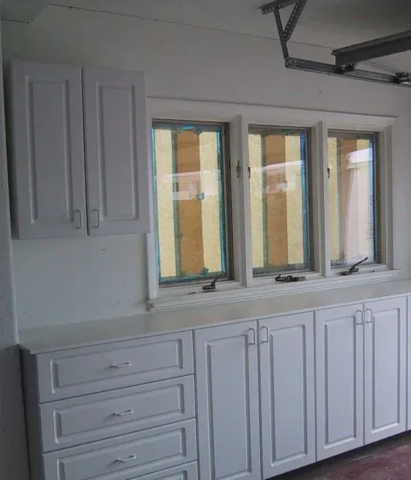 A kitchen with white cabinets and drawers and three windows.