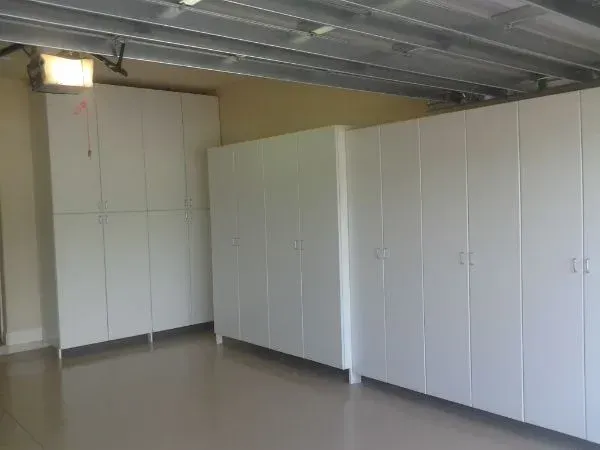 A garage with lots of white cabinets and a garage door open