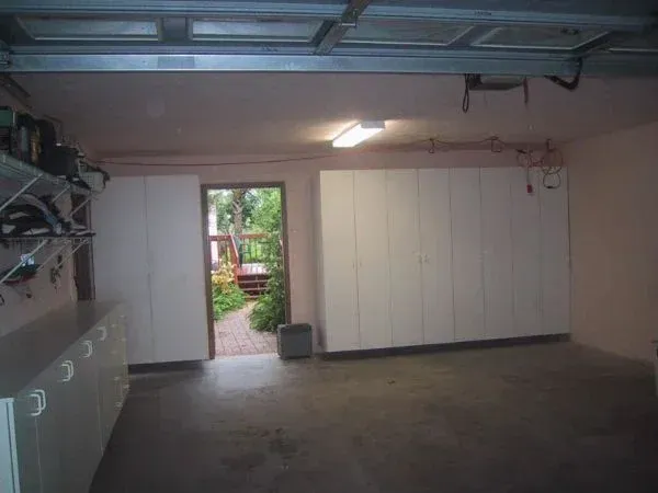 An empty garage with white cabinets and a garage door open.