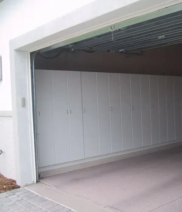 A garage with lots of white cabinets and a door open.