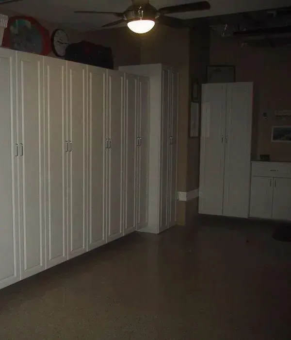 A garage with a lot of white cabinets and a ceiling fan.