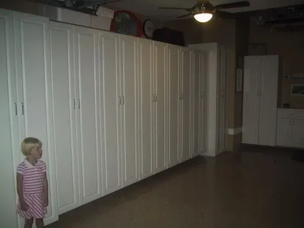 A little girl is standing in a room with a lot of white cabinets.