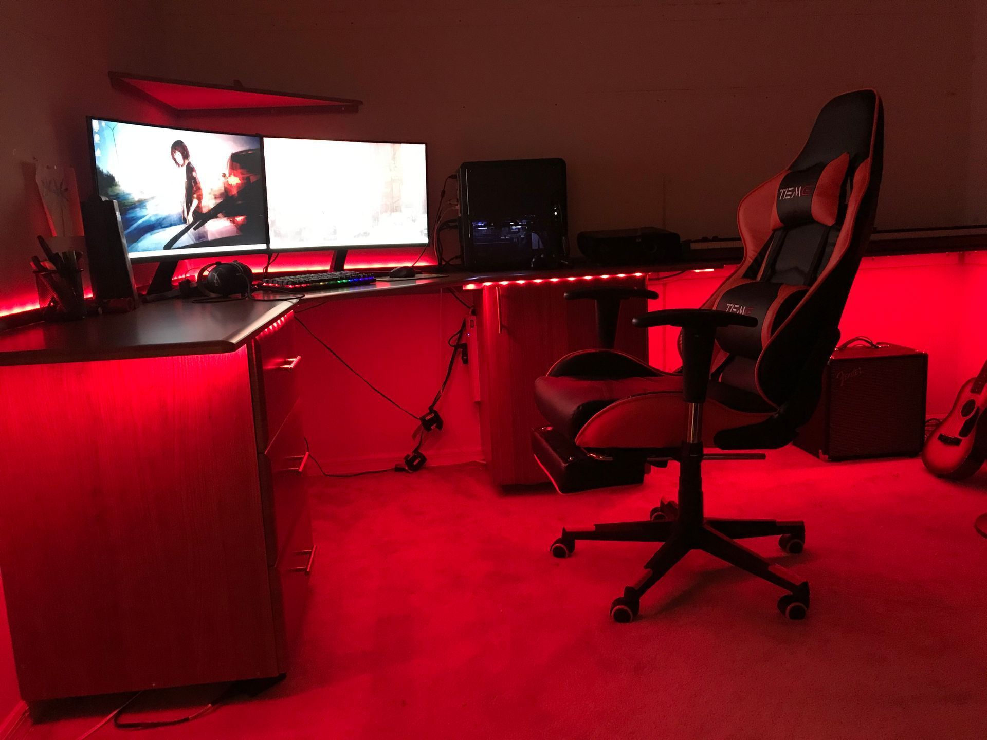 A computer desk with two monitors and a chair in a room with red lights