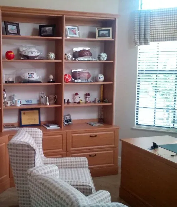 A room with a desk a chair and shelves full of sports memorabilia